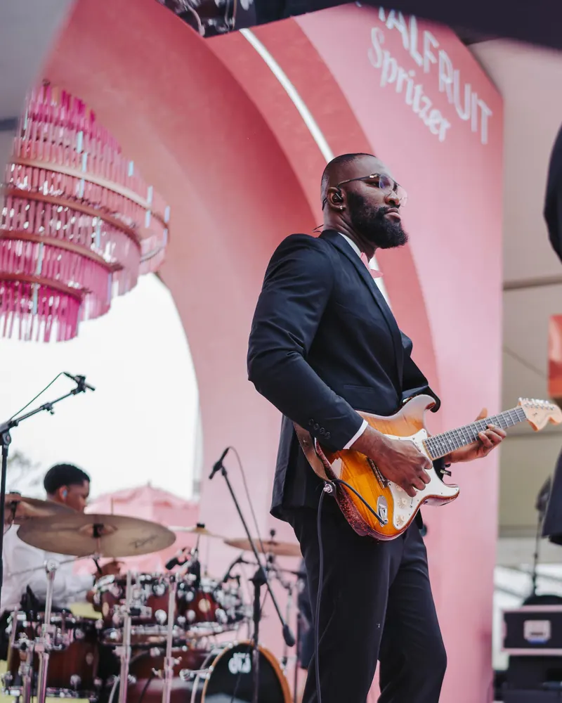 Iyke M Abu in a suit playing a sunburst Stratocaster on an outdoor stage